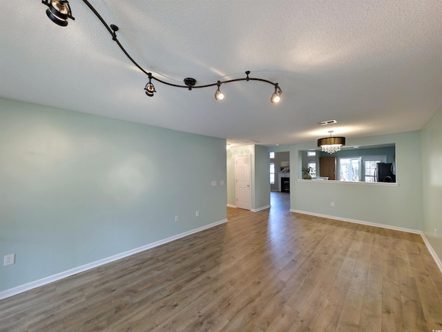 unfurnished living room with an inviting chandelier, a textured ceiling, baseboards, and wood finished floors