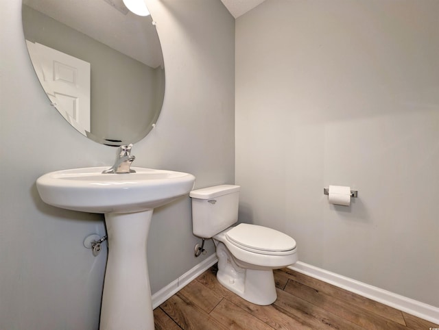 half bath with wood finished floors, toilet, and baseboards