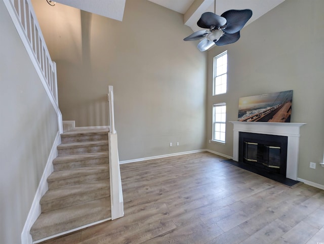 unfurnished living room featuring baseboards, a glass covered fireplace, a towering ceiling, stairs, and light wood-type flooring