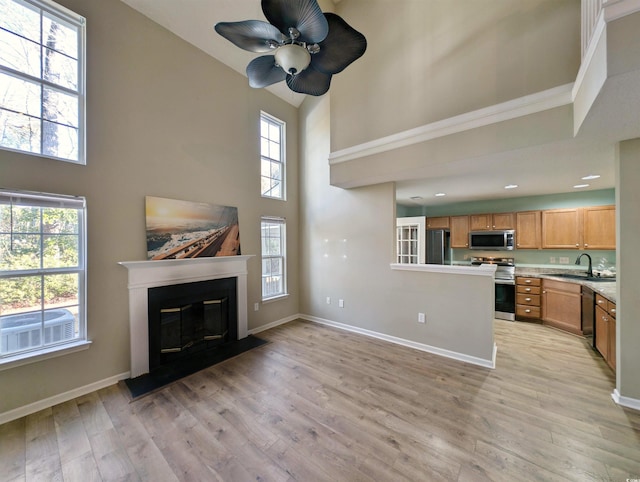 unfurnished living room featuring baseboards, plenty of natural light, a glass covered fireplace, and light wood-style floors