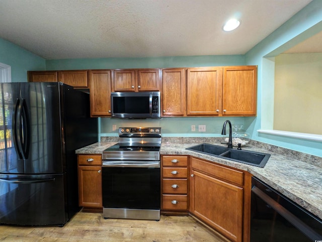 kitchen featuring light wood-style flooring, a sink, light countertops, brown cabinets, and black appliances