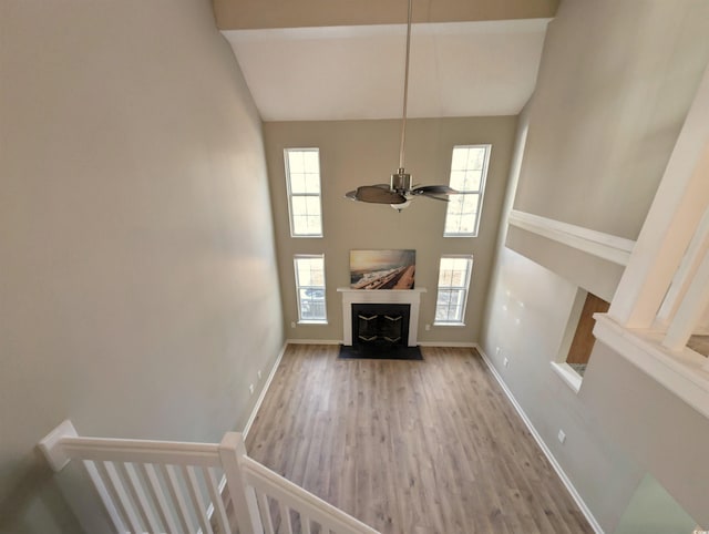 unfurnished living room featuring ceiling fan, wood finished floors, a fireplace with flush hearth, a towering ceiling, and baseboards