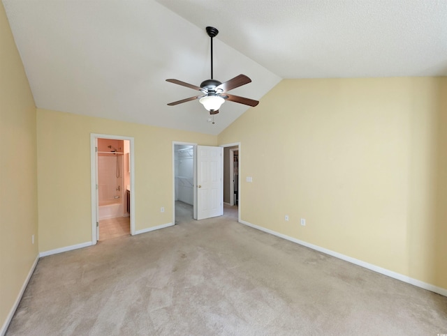 unfurnished bedroom featuring light carpet, baseboards, ensuite bath, vaulted ceiling, and a walk in closet