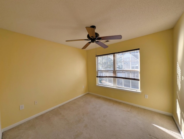 empty room featuring light colored carpet, ceiling fan, a textured ceiling, and baseboards