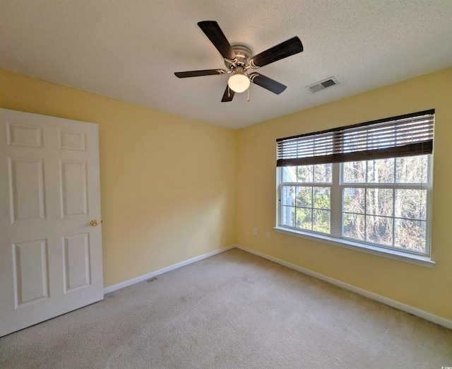 empty room with a textured ceiling, light carpet, a ceiling fan, visible vents, and baseboards