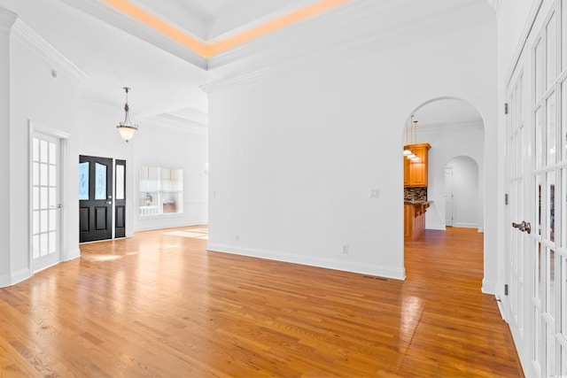 unfurnished living room featuring french doors, light wood-type flooring, ornamental molding, a raised ceiling, and a high ceiling