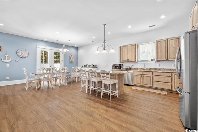 kitchen featuring appliances with stainless steel finishes, decorative light fixtures, a center island, and light hardwood / wood-style flooring