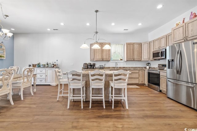 kitchen featuring light brown cabinetry, decorative light fixtures, stainless steel appliances, an inviting chandelier, and light hardwood / wood-style flooring