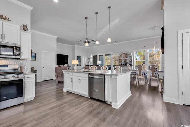 kitchen with white cabinetry, appliances with stainless steel finishes, decorative light fixtures, and a center island with sink