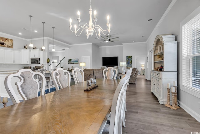 dining room featuring ceiling fan with notable chandelier, wood finished floors, visible vents, stairs, and ornamental molding