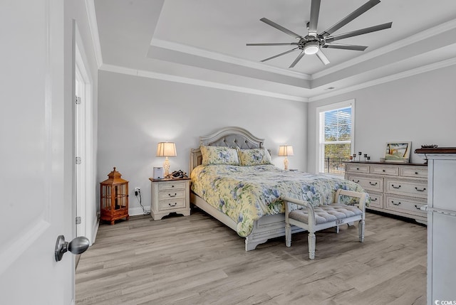 bedroom with light wood-type flooring, baseboards, a raised ceiling, and crown molding