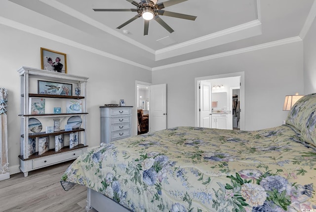 bedroom featuring connected bathroom, ornamental molding, ceiling fan, a tray ceiling, and light hardwood / wood-style flooring