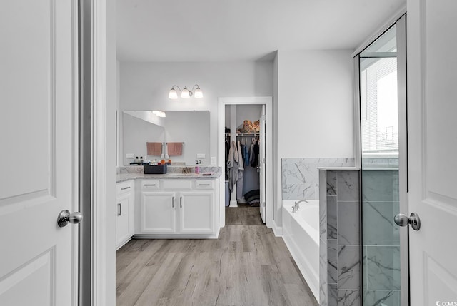 full bath featuring a bath, a spacious closet, wood finished floors, and vanity