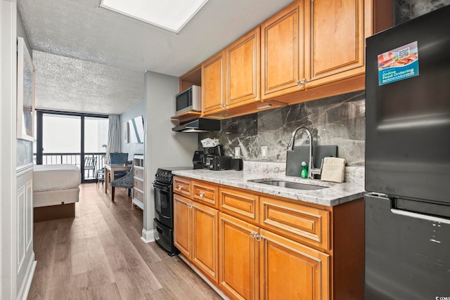 kitchen with sink, appliances with stainless steel finishes, backsplash, light stone counters, and light wood-type flooring