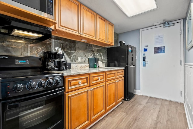 kitchen featuring sink, backsplash, black appliances, light hardwood / wood-style floors, and light stone countertops