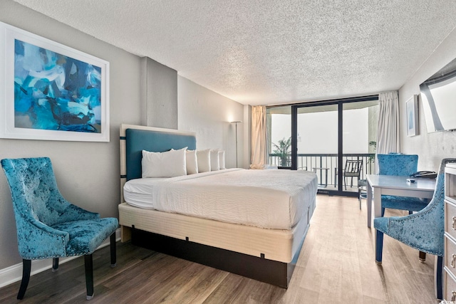 bedroom with hardwood / wood-style flooring, access to outside, a textured ceiling, and a wall of windows