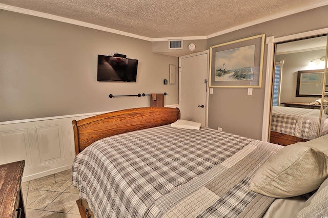 bedroom featuring wainscoting, visible vents, a decorative wall, and a textured ceiling