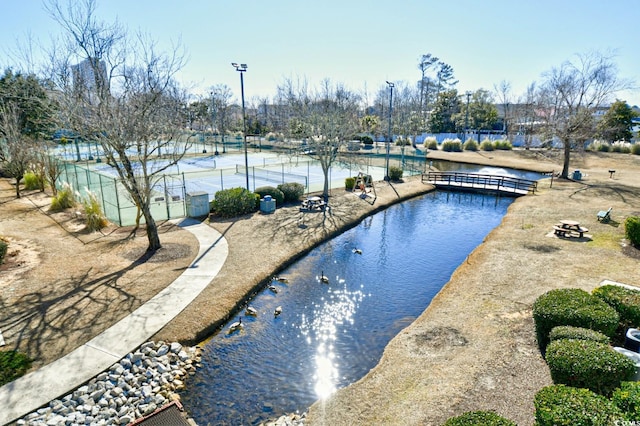 view of swimming pool featuring tennis court and a water view