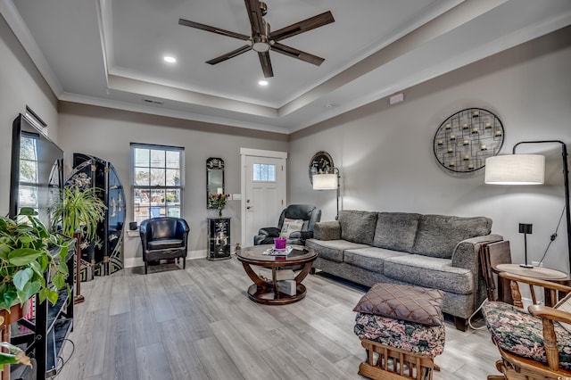 living room featuring light hardwood / wood-style flooring, ornamental molding, a raised ceiling, and ceiling fan