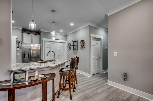 kitchen featuring stainless steel fridge with ice dispenser, sink, hanging light fixtures, light hardwood / wood-style floors, and light stone counters