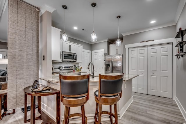 kitchen featuring pendant lighting, white cabinets, a kitchen bar, stainless steel appliances, and light stone countertops