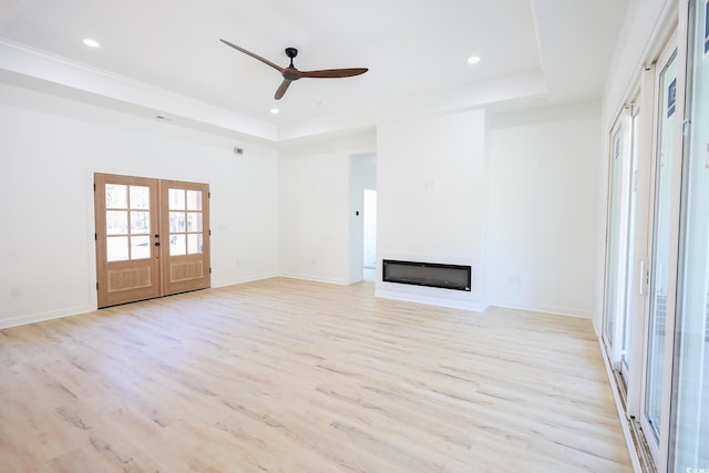 unfurnished living room featuring light wood-type flooring, a raised ceiling, ceiling fan, and french doors