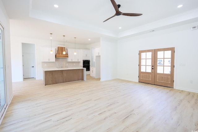 kitchen featuring white cabinetry, a tray ceiling, custom range hood, a center island with sink, and decorative light fixtures