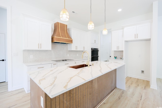 kitchen with sink, hanging light fixtures, wall chimney range hood, a kitchen island with sink, and white cabinets