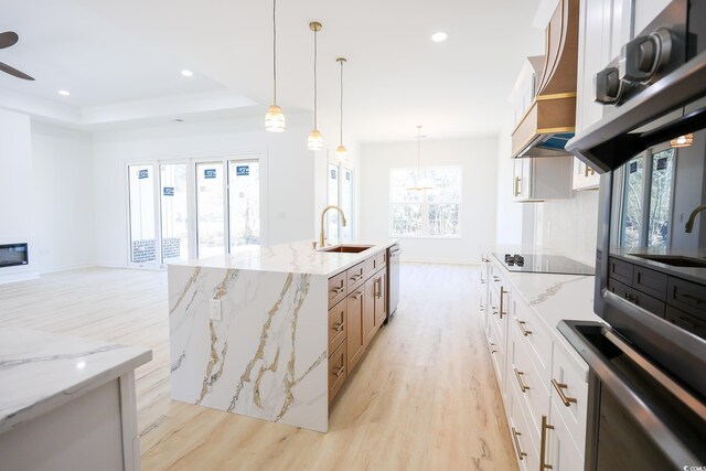 kitchen featuring dishwasher, white cabinetry, sink, light stone countertops, and a center island with sink