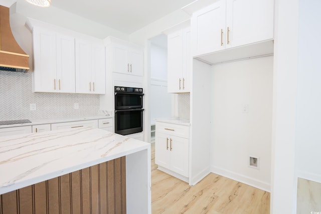 kitchen featuring premium range hood, white cabinets, decorative backsplash, light stone counters, and black appliances