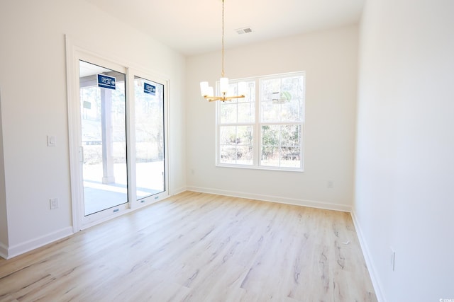 spare room with a notable chandelier, plenty of natural light, and light wood-type flooring