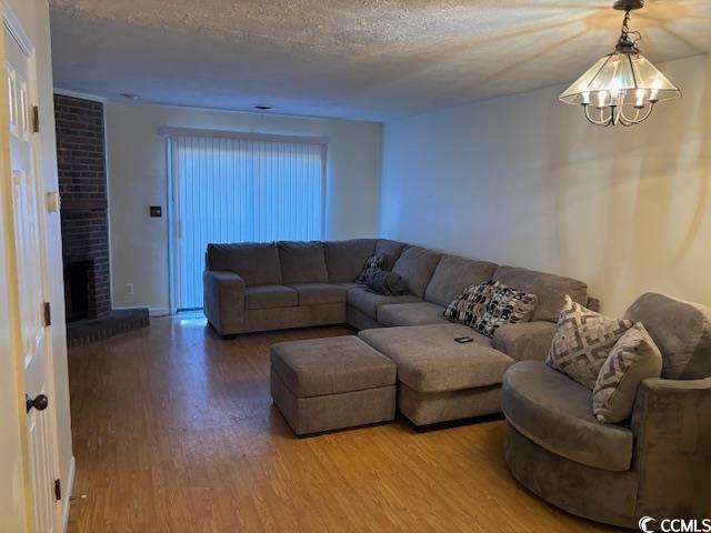 living room featuring a chandelier, a fireplace, a textured ceiling, and wood finished floors