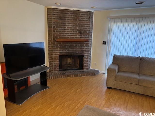 living room featuring baseboards, a fireplace, visible vents, and wood finished floors