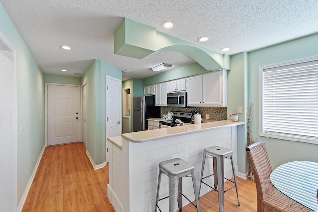 kitchen featuring appliances with stainless steel finishes, white cabinetry, tasteful backsplash, a kitchen bar, and kitchen peninsula