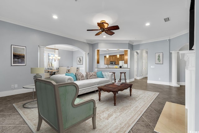 living room with crown molding, dark tile patterned floors, ceiling fan with notable chandelier, and ornate columns