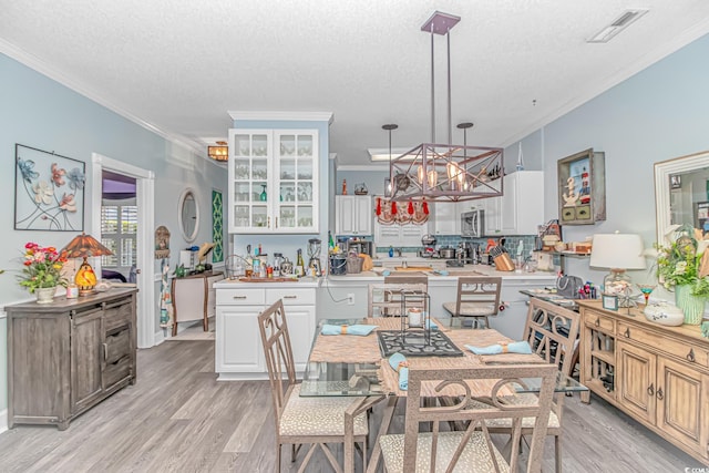 dining area with ornamental molding, an inviting chandelier, a textured ceiling, and light hardwood / wood-style floors