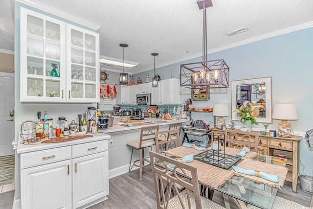 kitchen with crown molding, light hardwood / wood-style flooring, pendant lighting, decorative backsplash, and white cabinets