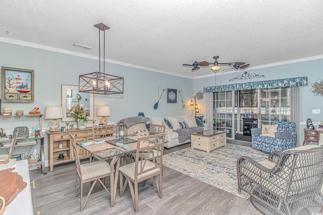 dining space featuring crown molding, hardwood / wood-style flooring, ceiling fan with notable chandelier, and a textured ceiling