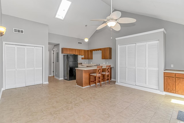 kitchen with visible vents, brown cabinets, freestanding refrigerator, light countertops, and under cabinet range hood