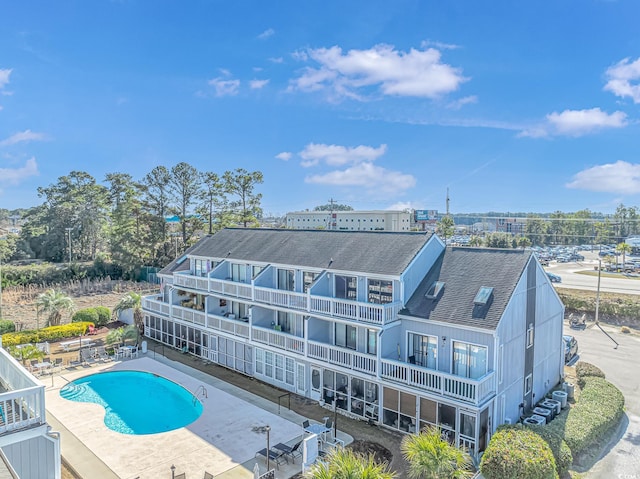 rear view of house featuring a shingled roof, a patio, a balcony, and a community pool