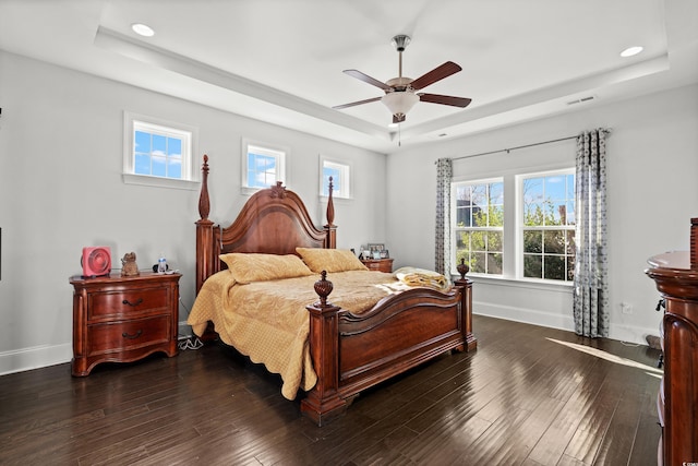 bedroom with dark wood-type flooring, ceiling fan, and a tray ceiling