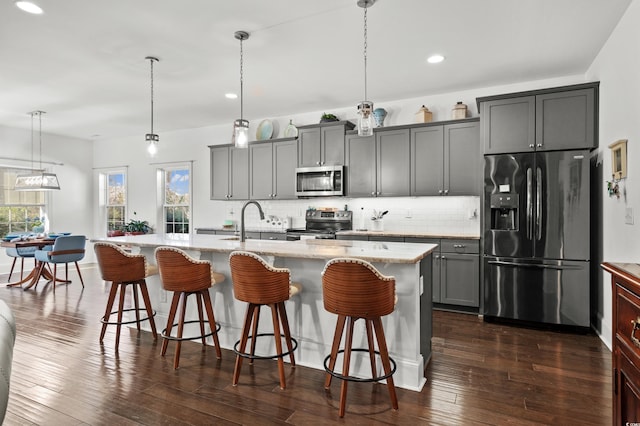 kitchen with a kitchen island with sink, decorative light fixtures, stainless steel appliances, and gray cabinetry