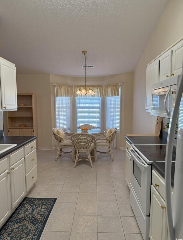 kitchen with light tile patterned flooring, vaulted ceiling, white cabinets, hanging light fixtures, and white appliances