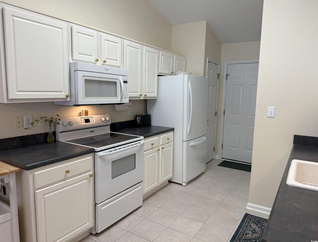 kitchen featuring white appliances, dark countertops, and white cabinets