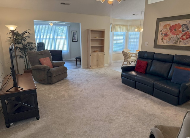 carpeted living room featuring visible vents, baseboards, and ceiling fan with notable chandelier