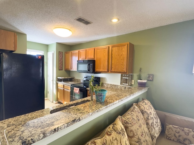 kitchen with a textured ceiling, a kitchen breakfast bar, kitchen peninsula, light stone countertops, and black appliances