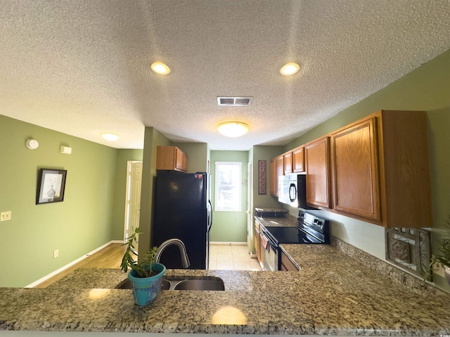 kitchen with stone countertops, electric range oven, black refrigerator, sink, and kitchen peninsula