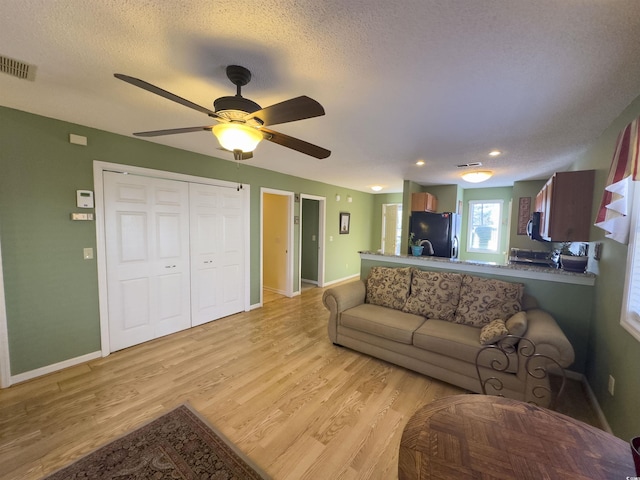 living room featuring ceiling fan, a textured ceiling, and light wood-type flooring