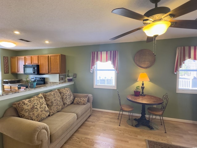 living room with ceiling fan, a textured ceiling, and light wood-type flooring