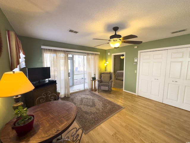 living room featuring ceiling fan, a textured ceiling, and light wood-type flooring